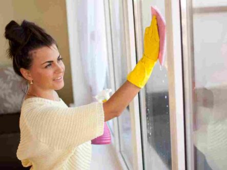 a woman cleaning windows wearing gloves.